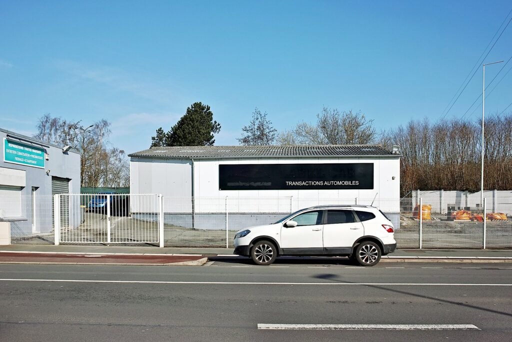 Garage de transactions automobiles en bord de route, avec un SUV blanc stationné devant le bâtiment sous un ciel bleu