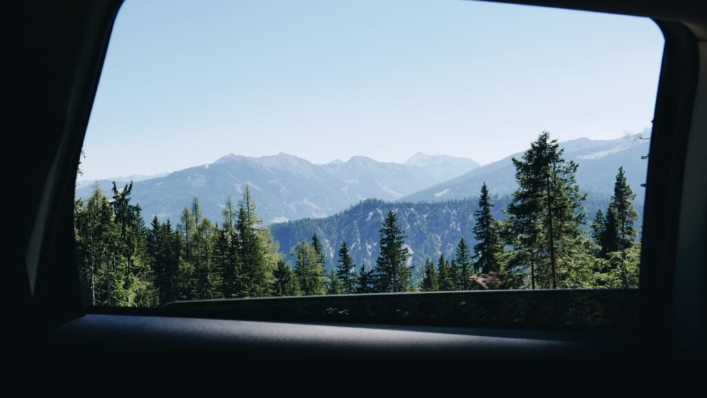 Paysage de montagnes et de sapins vu par la vitre arrière d’une voiture pendant un trajet en famille