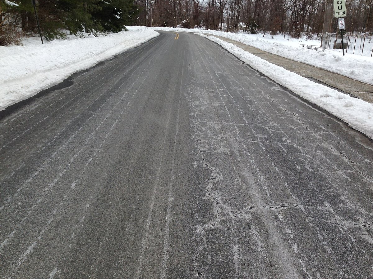 Route enneigée traitée à la saumure : traînées de sel blanches séchées sur l’asphalte avant une chute de neige