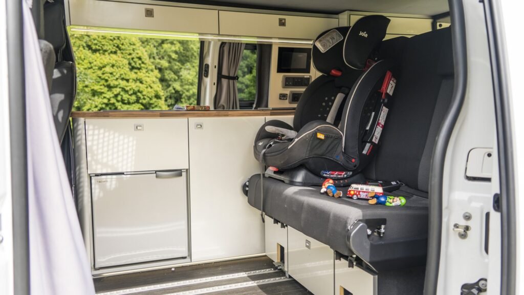 Siège auto pour enfant installé à l’arrière d’un véhicule utilitaire, près d’une vitre latérale et de jouets, photo d’illustration de la zone passagers arrière