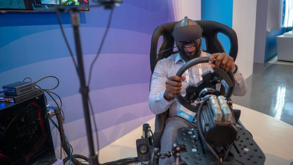 Un homme coiffé d’un casque de réalité virtuelle tient le volant d’un simulateur de conduite sur un salon, illustration des simulateurs et du permis de conduire