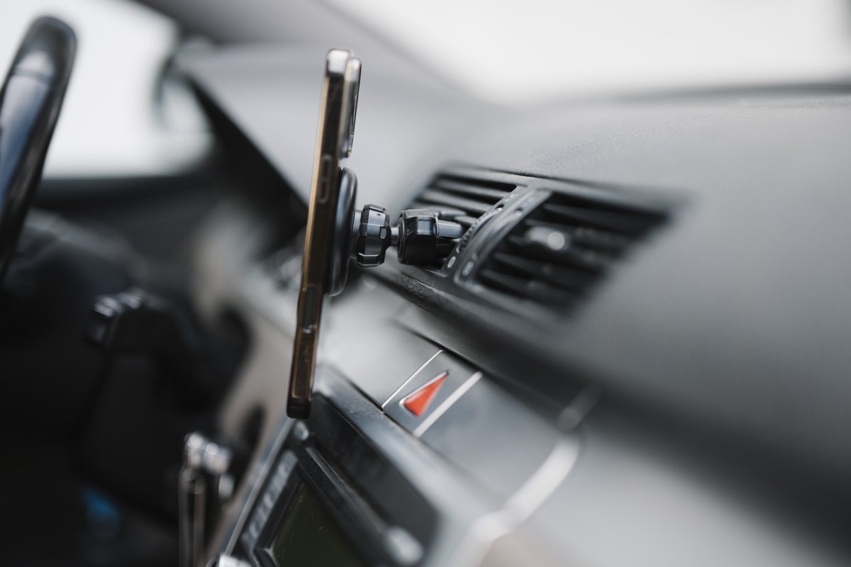 Smartphone fixé sur un support aimanté à la grille d’aération d’une voiture, tableau de bord gris flou à l’arrière-plan