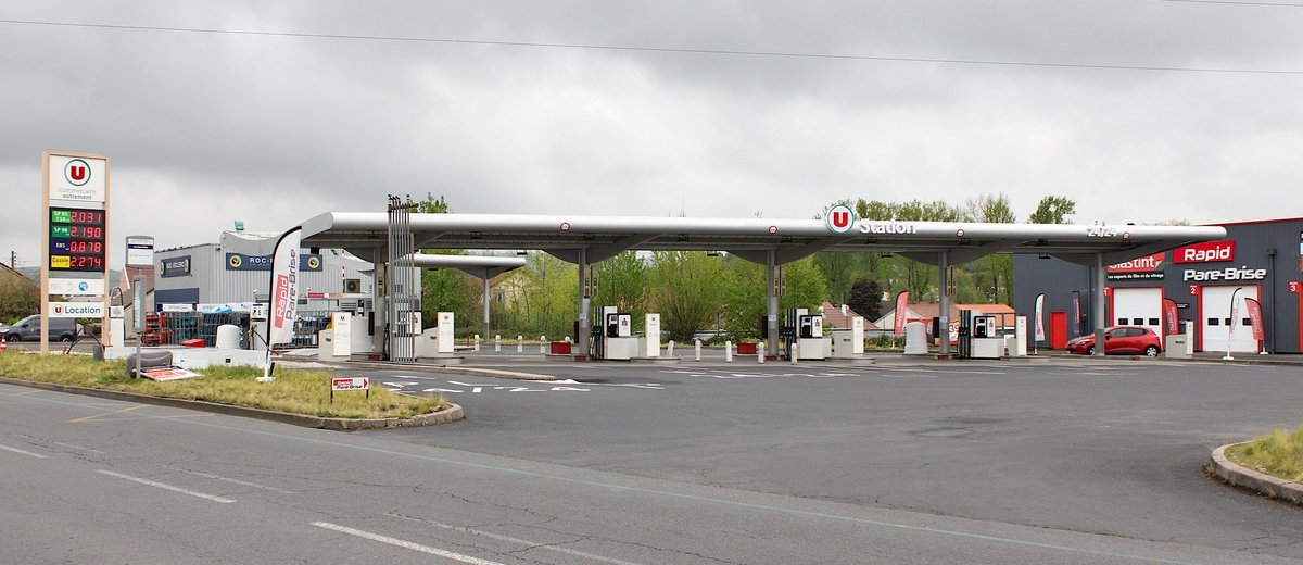 Station-service d’un magasin U à Cusset, avec son totem de prix des carburants à gauche, ses pompes sous un grand auvent blanc et un ciel gris