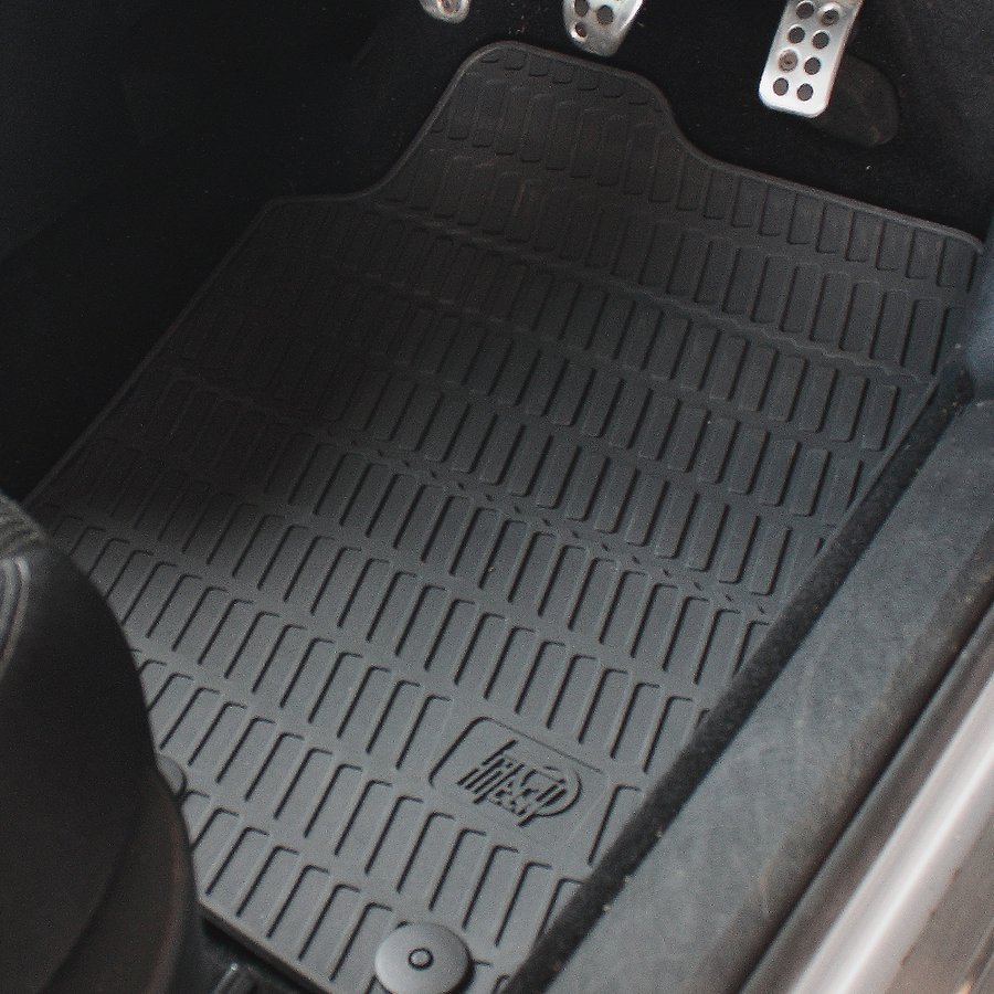 Tapis de voiture en caoutchouc sur mesure côté conducteur, avec ses rainures, son logo moulé et un clip de fixation rond en bas, sous des pédales en aluminium perforé