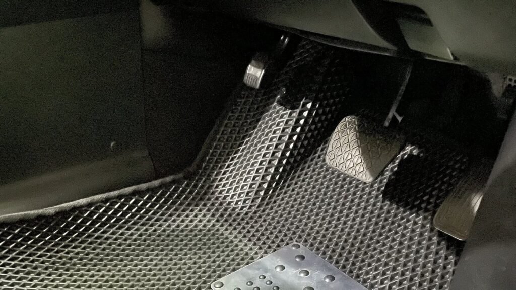 Plancher côté conducteur d’une voiture équipé d’un tapis noir alvéolé en EVA avec une talonnette métallique, au pied des pédales de frein et d’accélérateur et du repose-pied