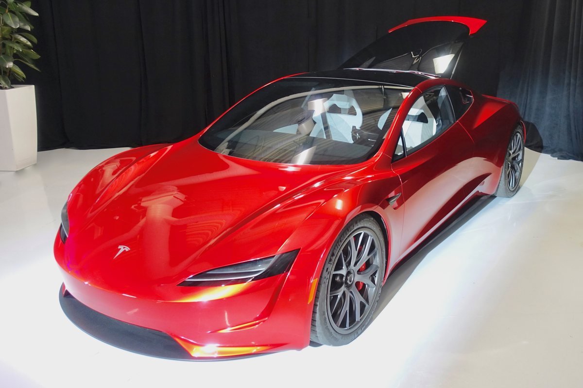 Prototype rouge du Tesla Roadster de deuxième génération exposé dans une salle aux rideaux noirs, panneau de toit soulevé