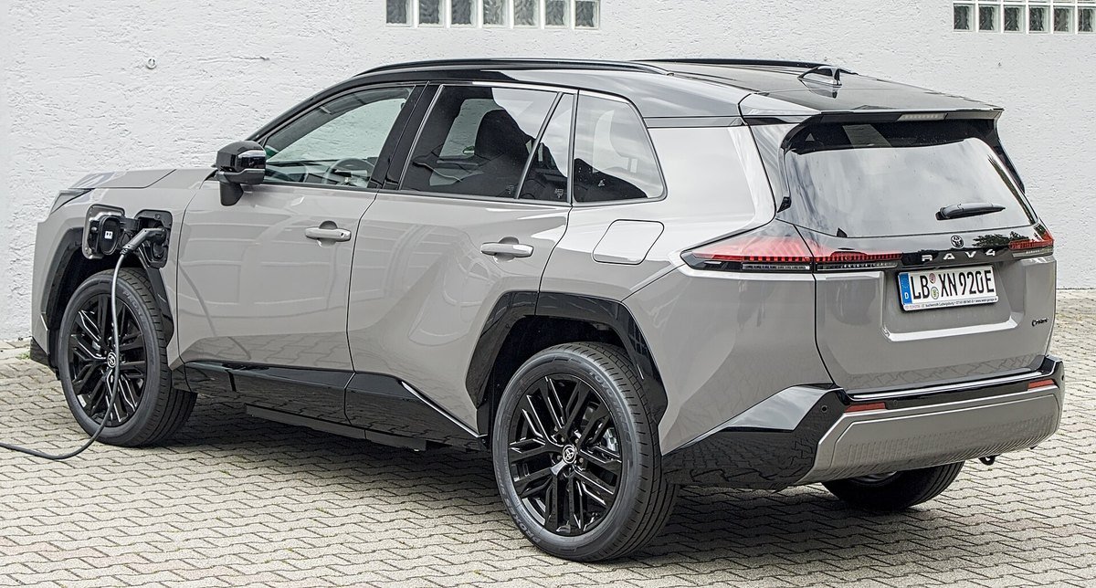 Toyota RAV4 hybride rechargeable de nouvelle génération, gris à toit noir, branché à un câble de recharge sur un parking pavé