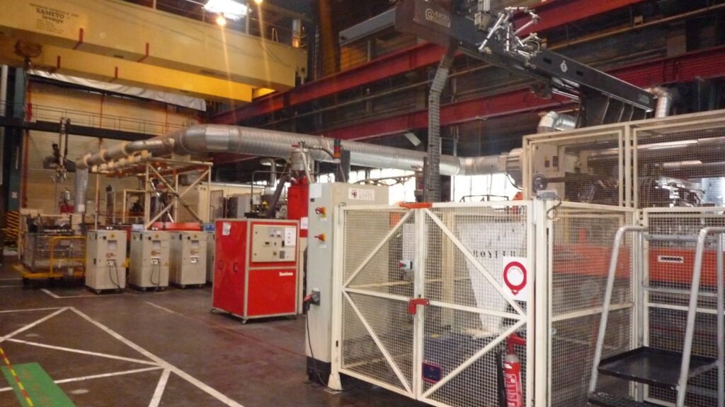 Intérieur de l’usine automobile Renault de Douai : machines industrielles, cages de protection blanches, pont roulant jaune Sameto et gaines métalliques au plafond