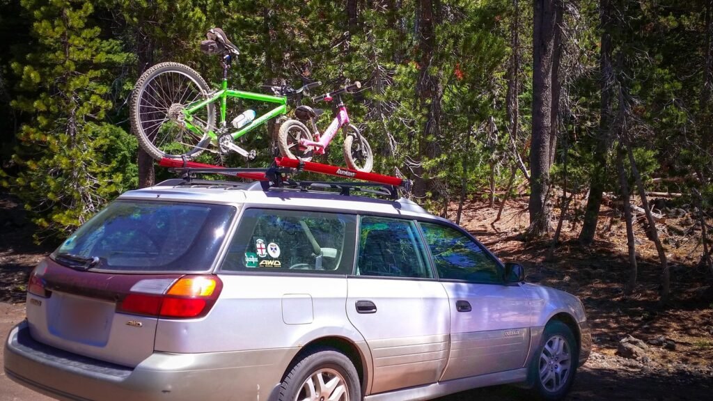 Break gris avec deux vélos fixés sur une galerie de toit, garé en forêt