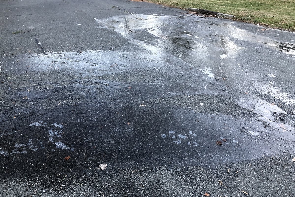 Plaque de verglas transparent et luisant sur une route goudronnée sombre, à peine visible sur l’asphalte