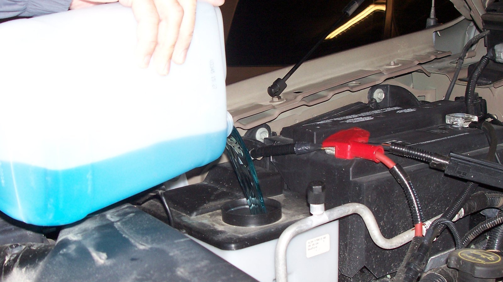 Liquide lave-glace bleu versé directement d’un bidon dans le réservoir sous le capot d’une voiture