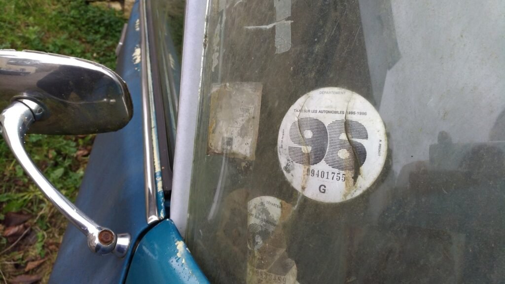 Ancienne vignette automobile française de 1996 collée sur le pare-brise d'une voiture bleue, rétroviseur chromé au premier plan