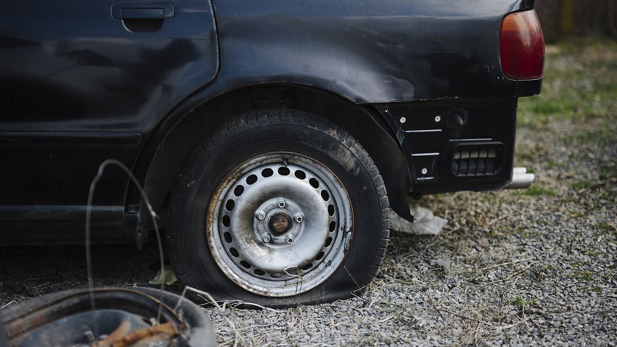 Voiture noire garée sur du gravier avec un pneu arrière complètement à plat
